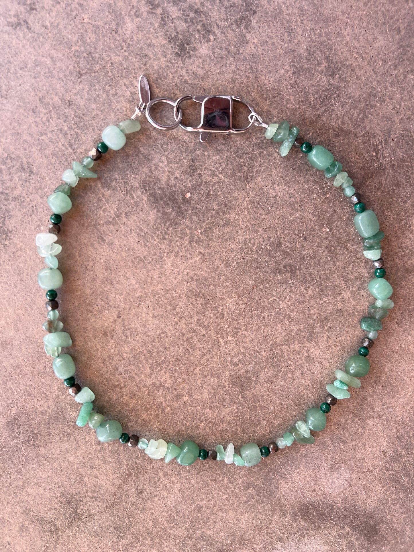 A green and black beaded necklace with a stainless steel clasp, displayed against a textured background.