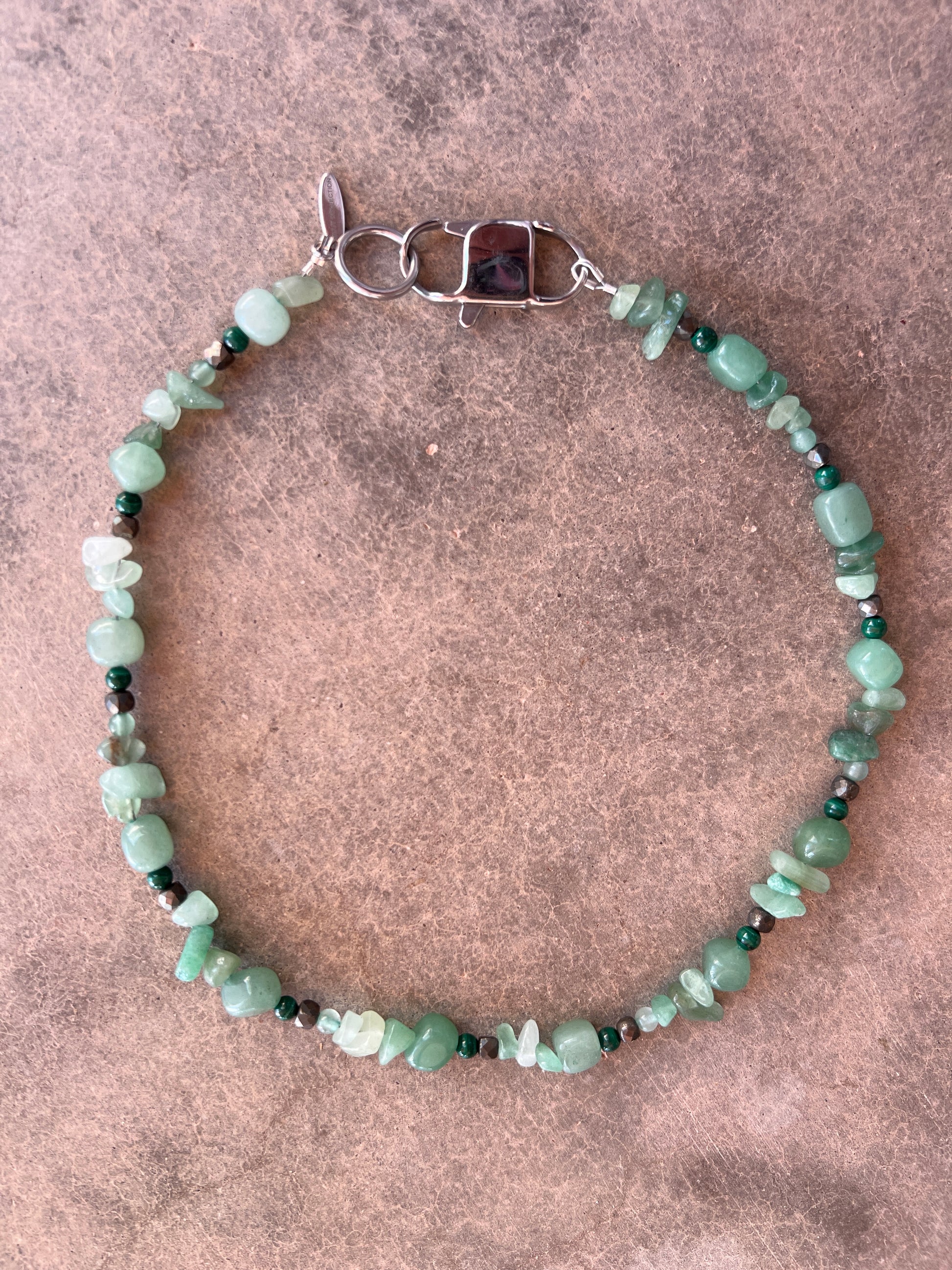 A green and black beaded necklace with a stainless steel clasp, displayed against a textured background.