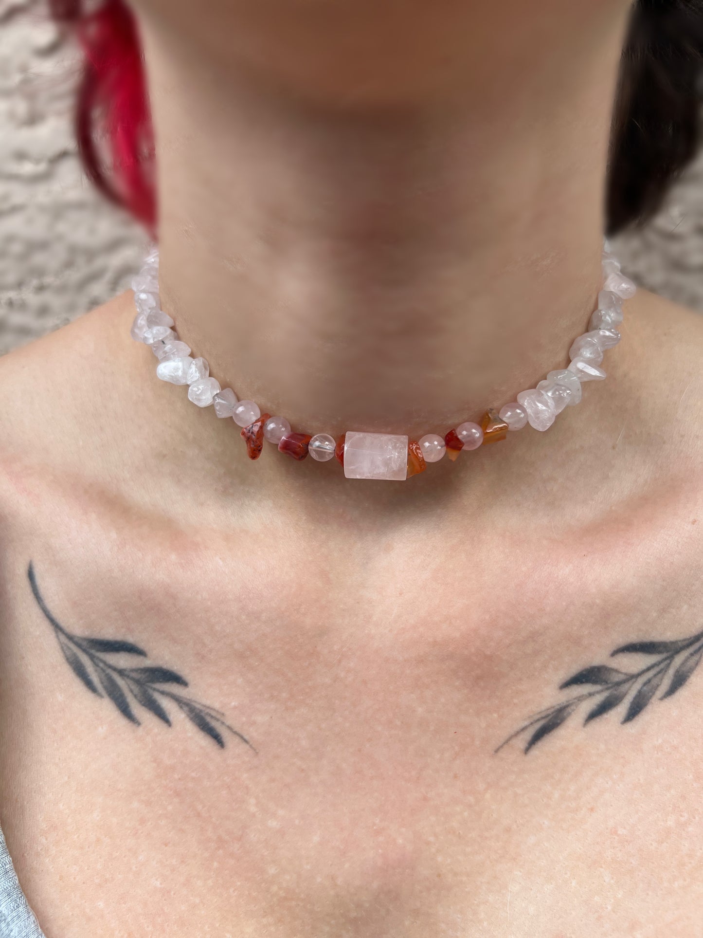 A person showcasing a sterling silver necklace with multicolored gemstones, specifically a rose quartz and carnelian, around their neck.