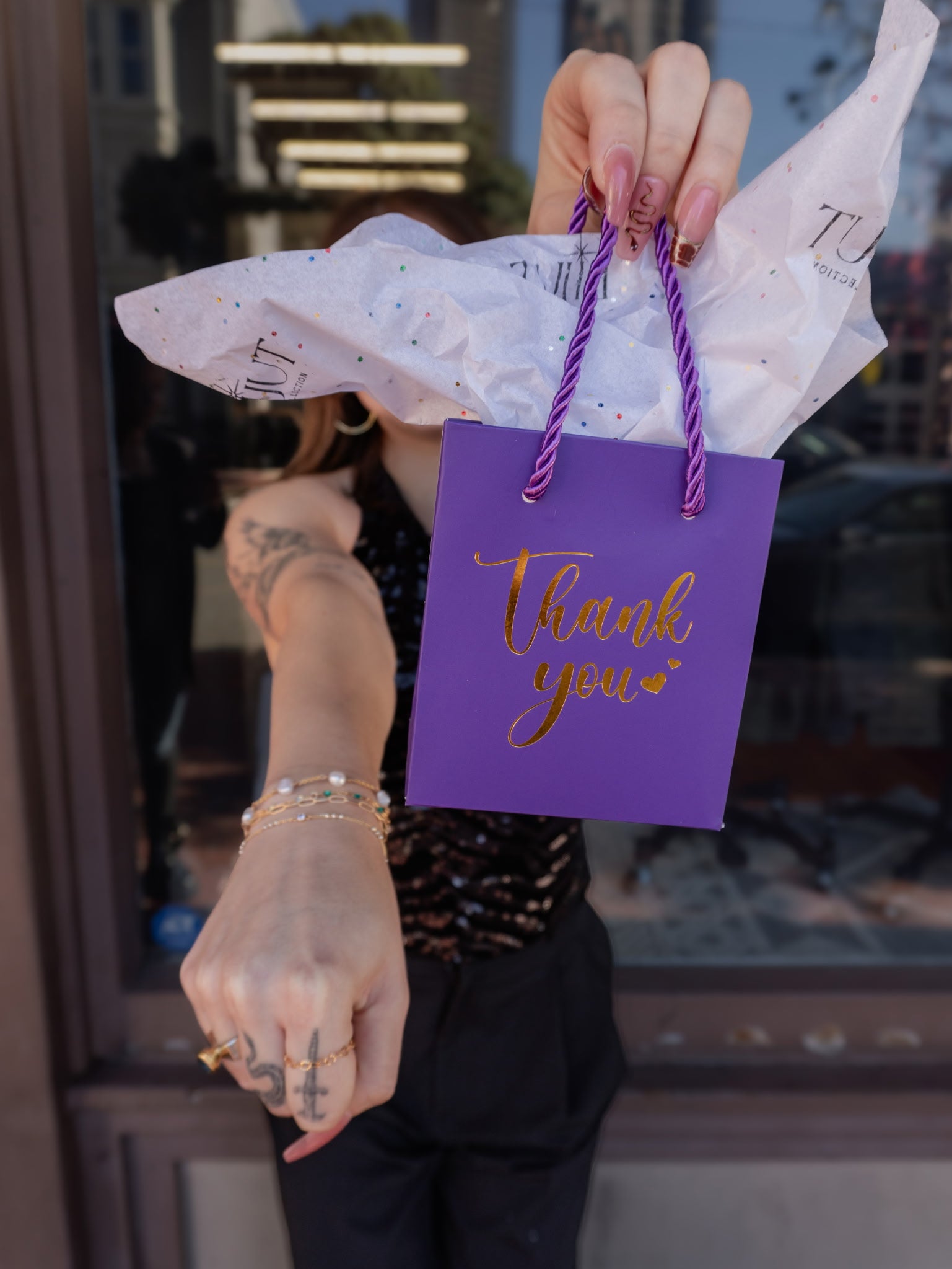 Purple gift bag with 'Thank you' text held by a person in an urban setting.
