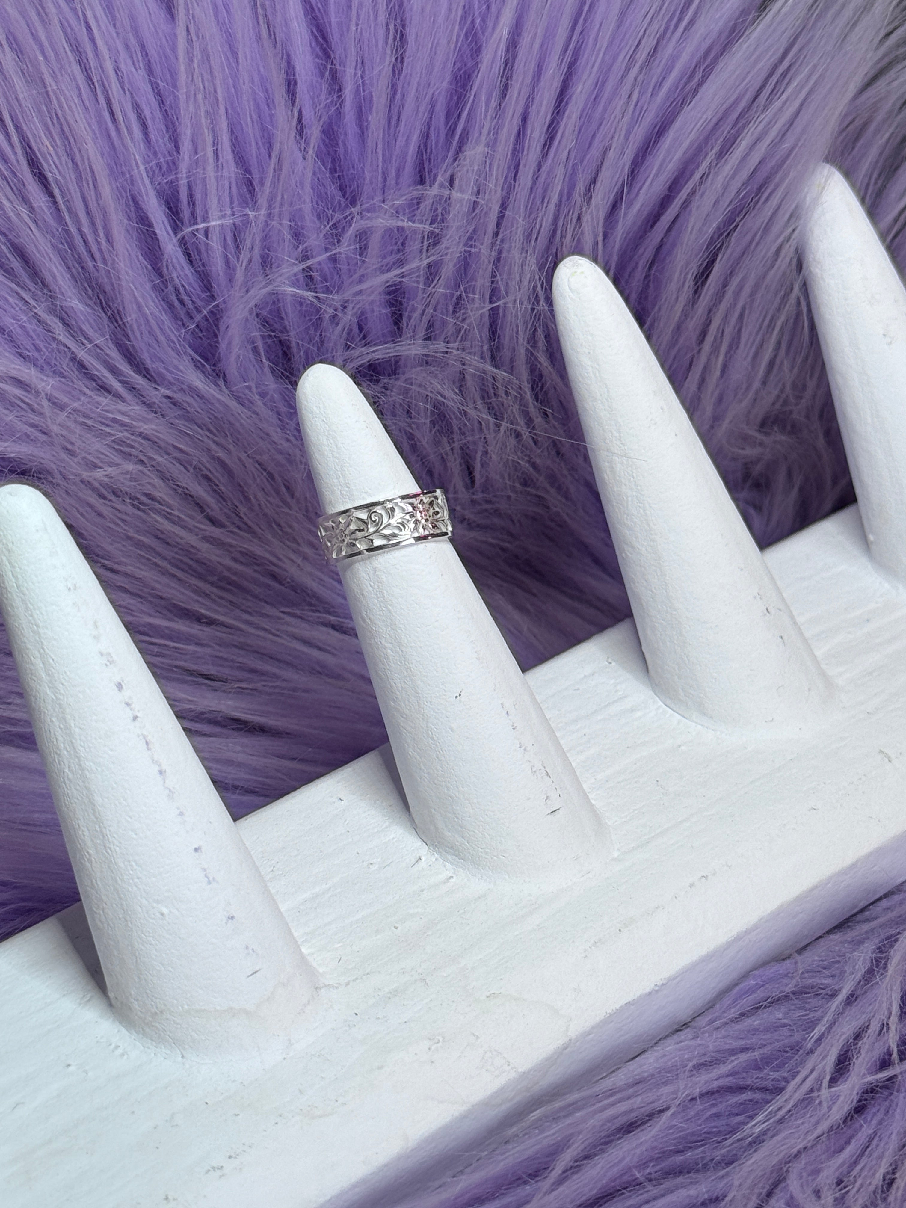 White mannequin hand with a silver ring on a purple textured background