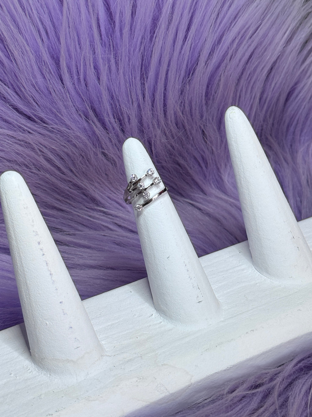 White stiletto nails with a silver ring on a purple fur background