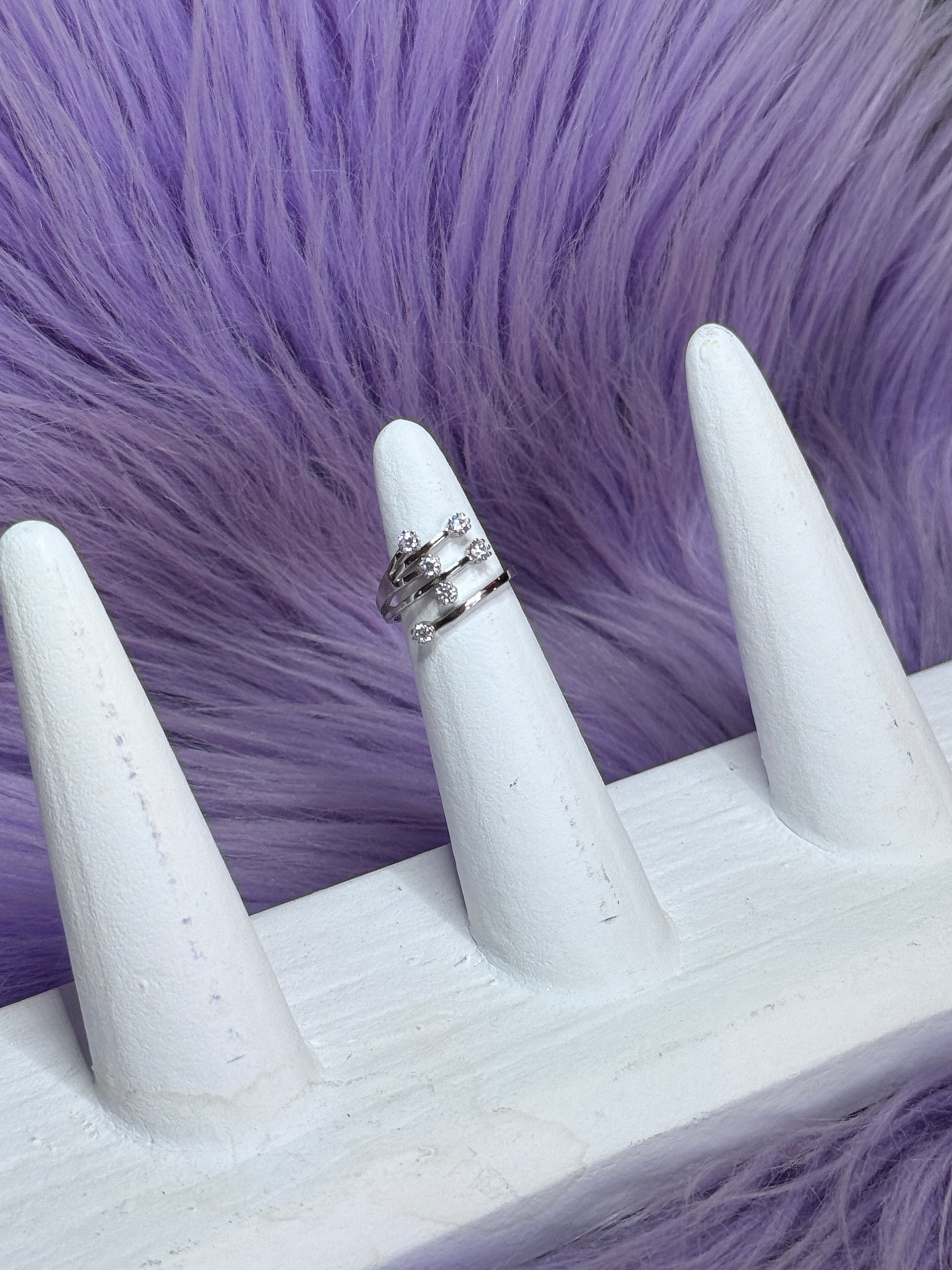 White stiletto nails with a silver ring on a purple fur background