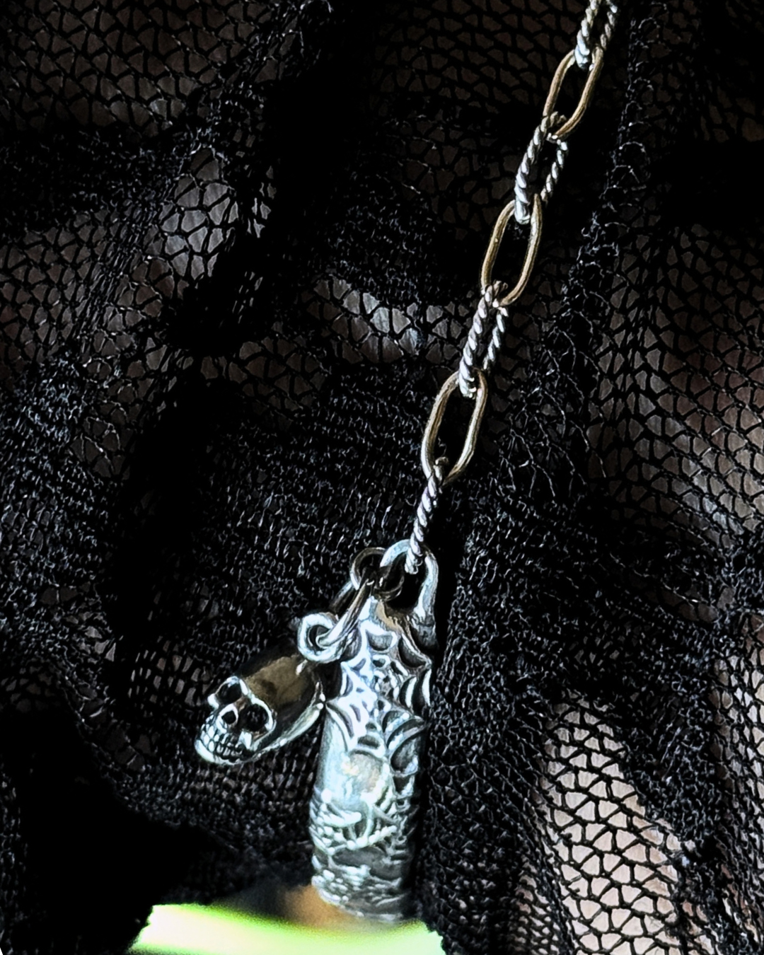 A gothic-style silver pendant necklace featuring a skull and a spiderwebbed female figure, displayed against a black lace background. Handcrafted sterling silver bangle with spider web design, skull charm, and mixed-metal chain.