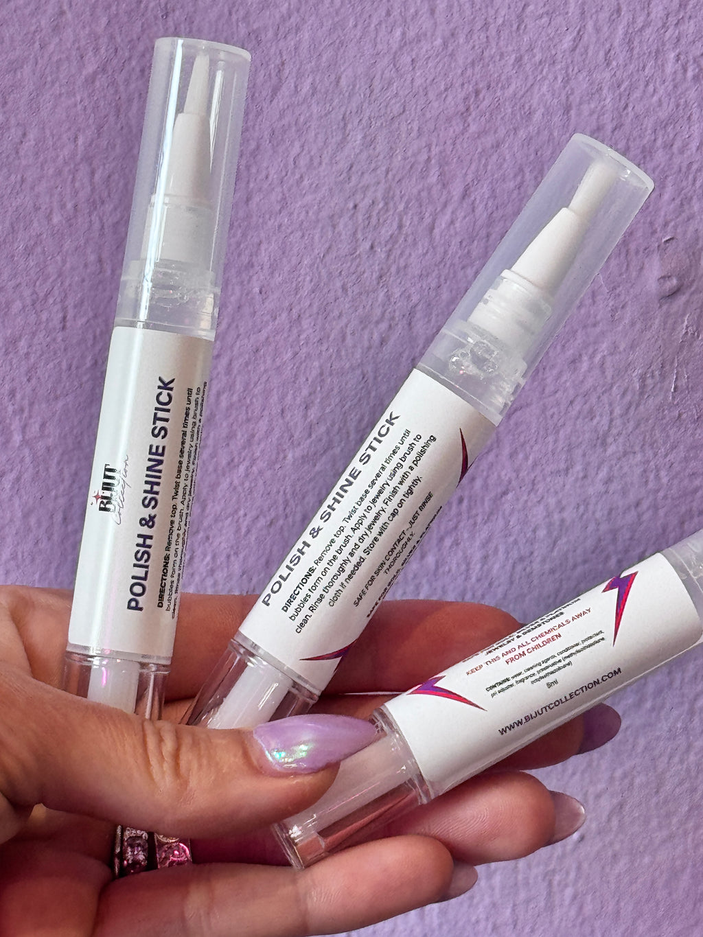 Hand holding three small POLISHING tubes with labels on a purple textured background FOR JEWELRY CLEANING 