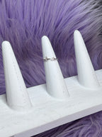 White stiletto nails with a silver ring on a purple fur background and smile written by ring