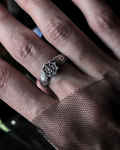 A close-up of a hand wearing a silver ring with an intricate spiderweb design, with black mesh fabric draped over the wrist.
