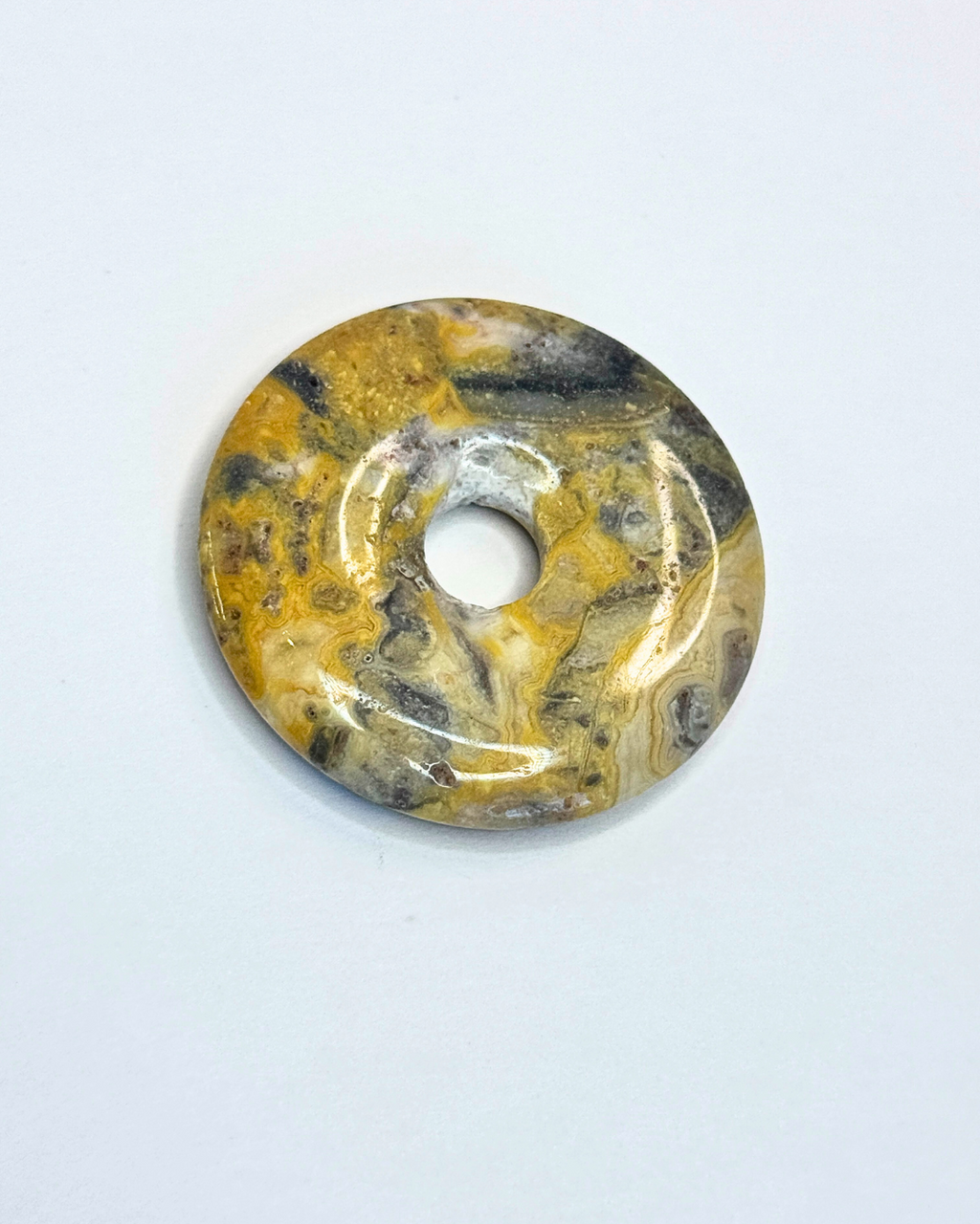 Round stone pendant with a central hole on a white background