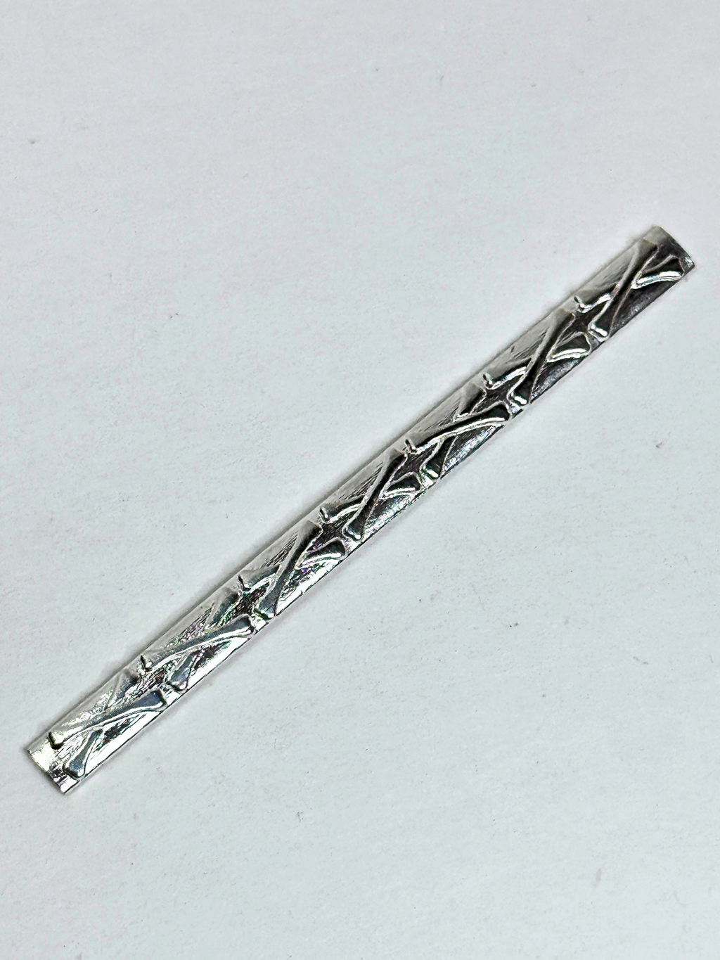 Silver tie clip with intricate design on a white background