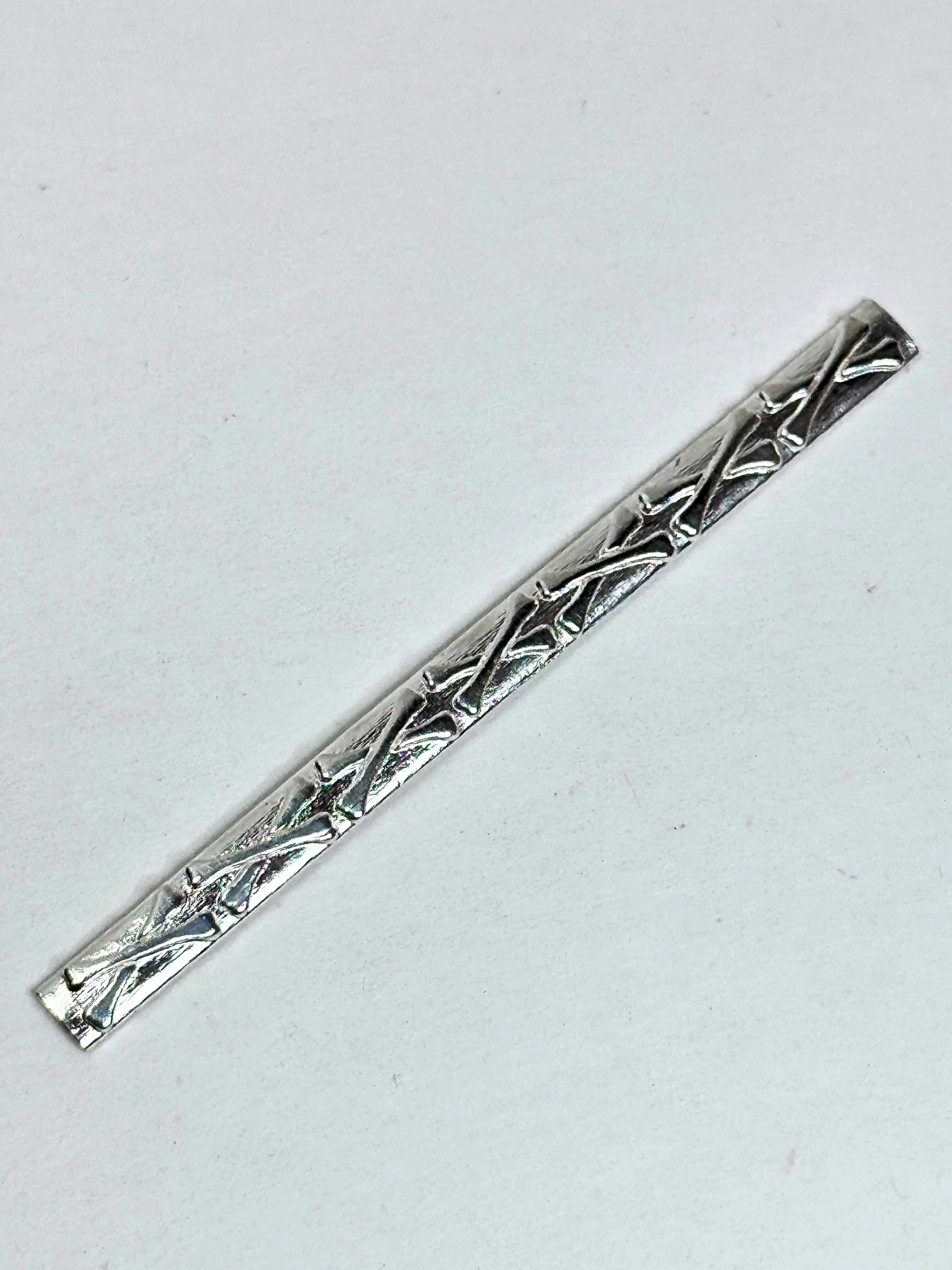 Silver tie clip with intricate design on a white background