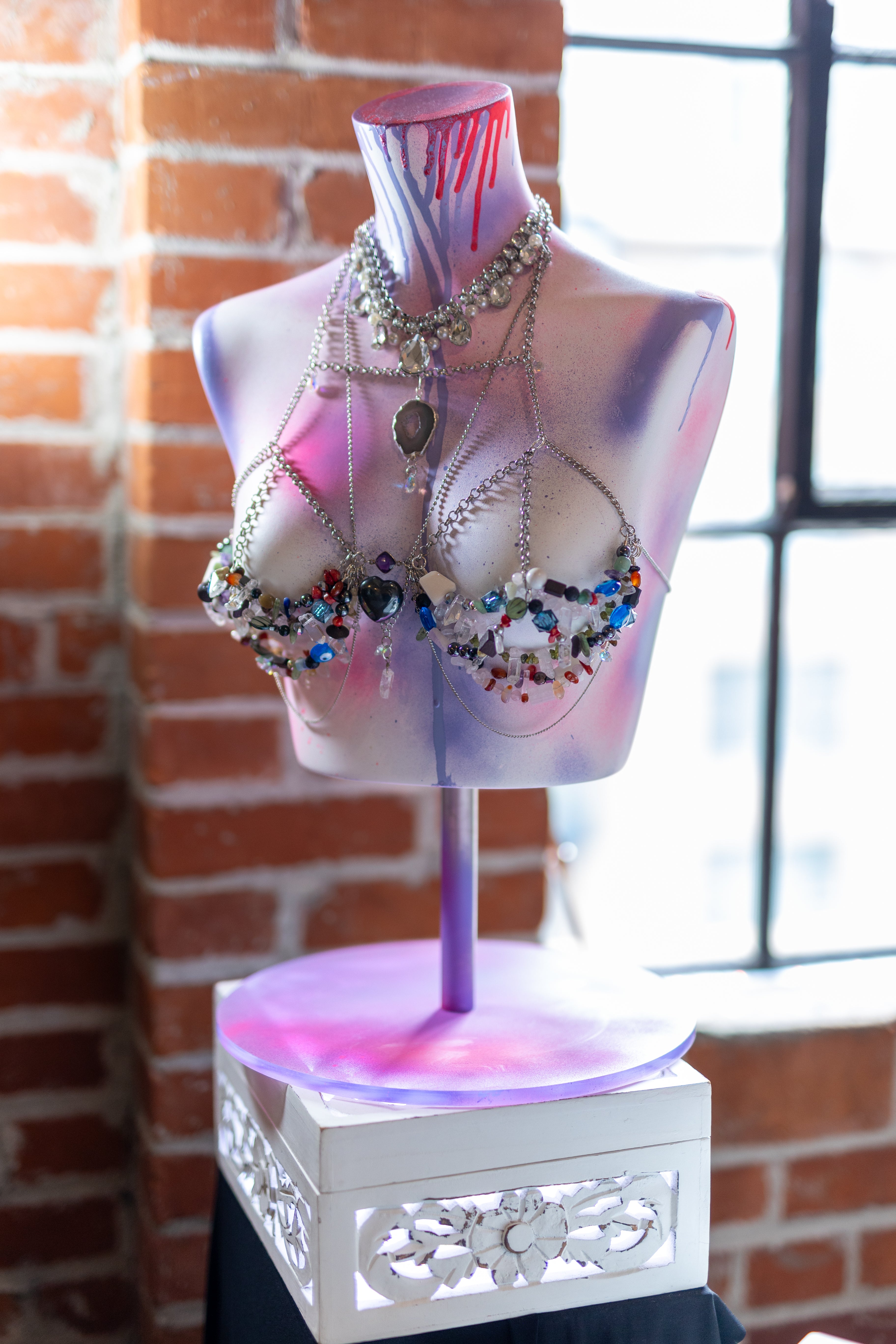 Mannequin torso with colorful jewelry display against a brick wall.