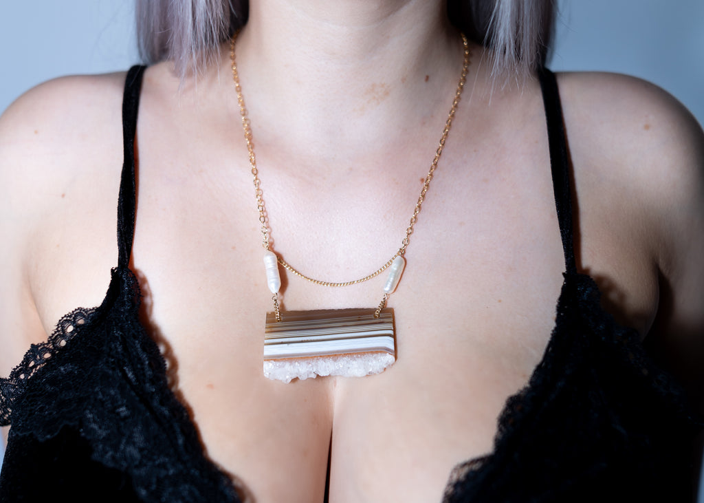 Person wearing a gold necklace with a rectangular pendant against a neutral background