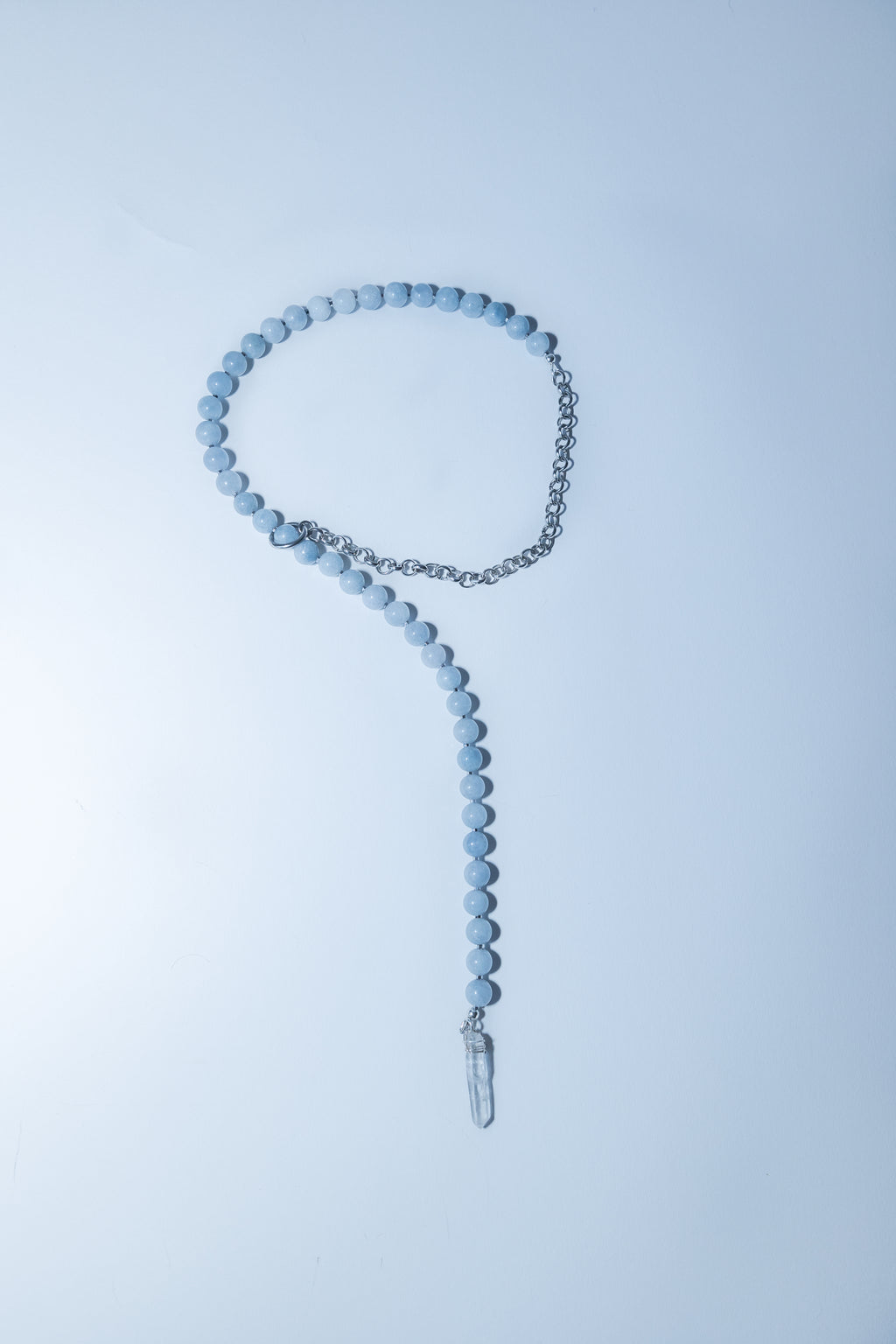 Necklace with blue beads and a clear crystal pendant on a light blue background
