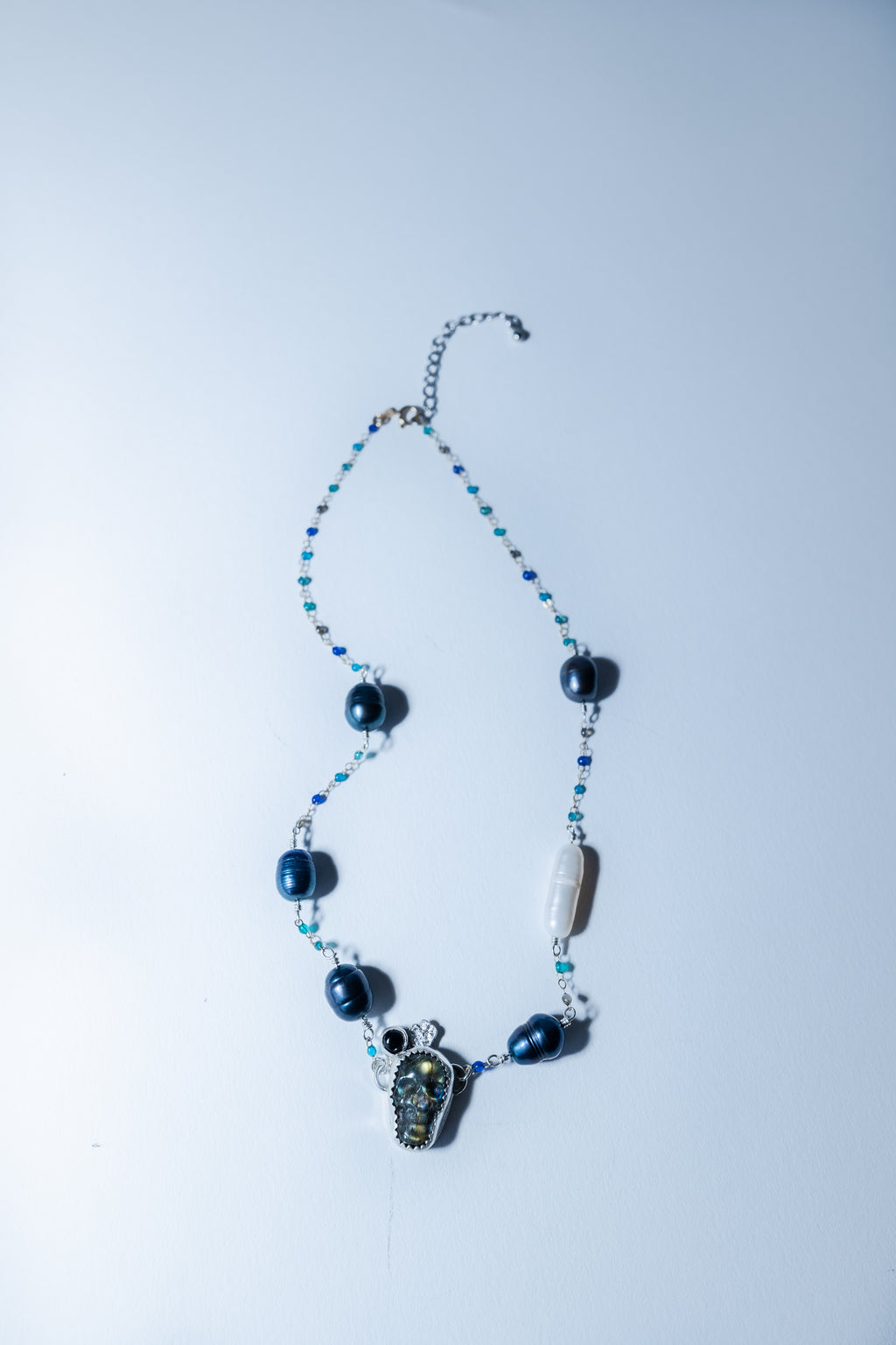 Necklace with blue beads and a skull pendant on a light gray background