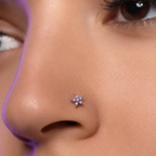 A close-up of a person's nose wearing a small flower-shaped nose stud with clear stones in a gold-tone setting.