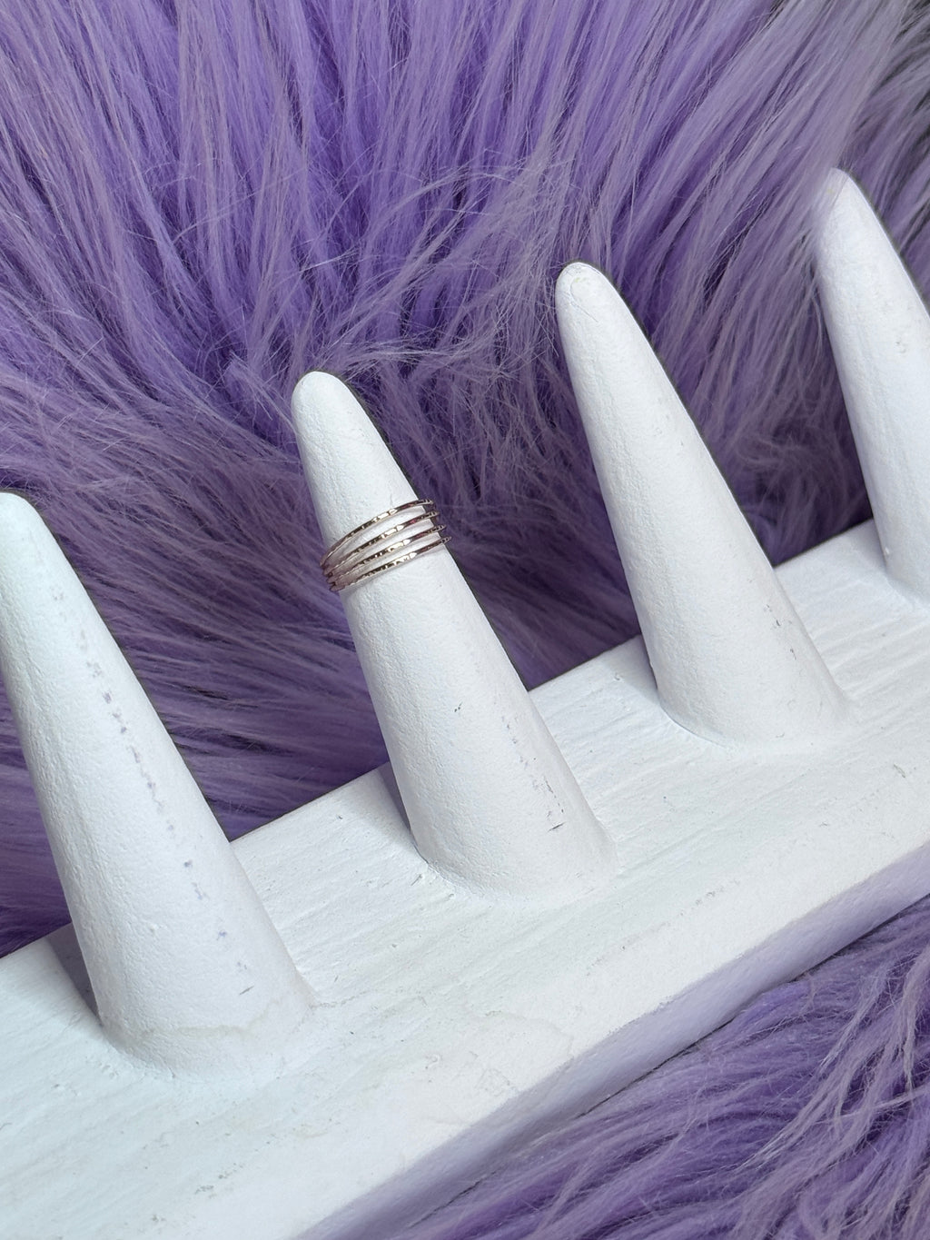 White ring on a mannequin finger against a purple fur background