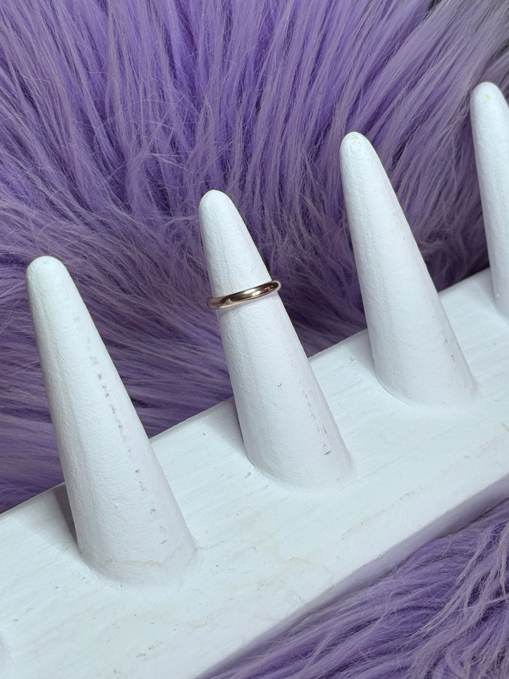 White mannequin hand with a gold ring on a purple fur background