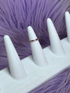 White mannequin hand with a gold ring on a purple fur background