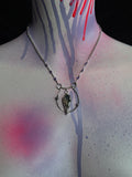 A silver chain necklace with a coffin moss agate pendant and small star charms, displayed on a mannequin torso decorated with spray-paint splatters and drips.