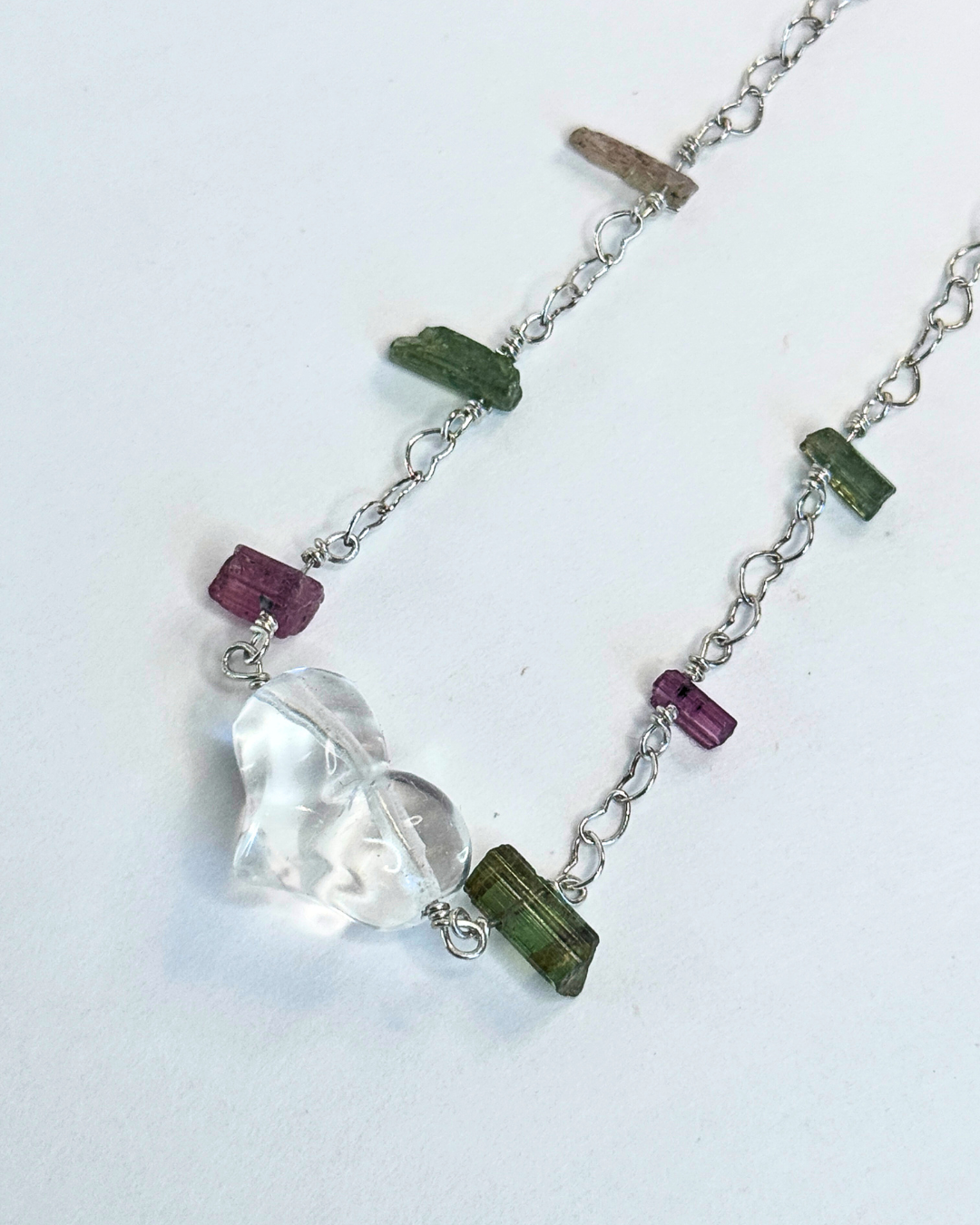 Necklace with a heart-shaped pendant and green and purple beads on a white background