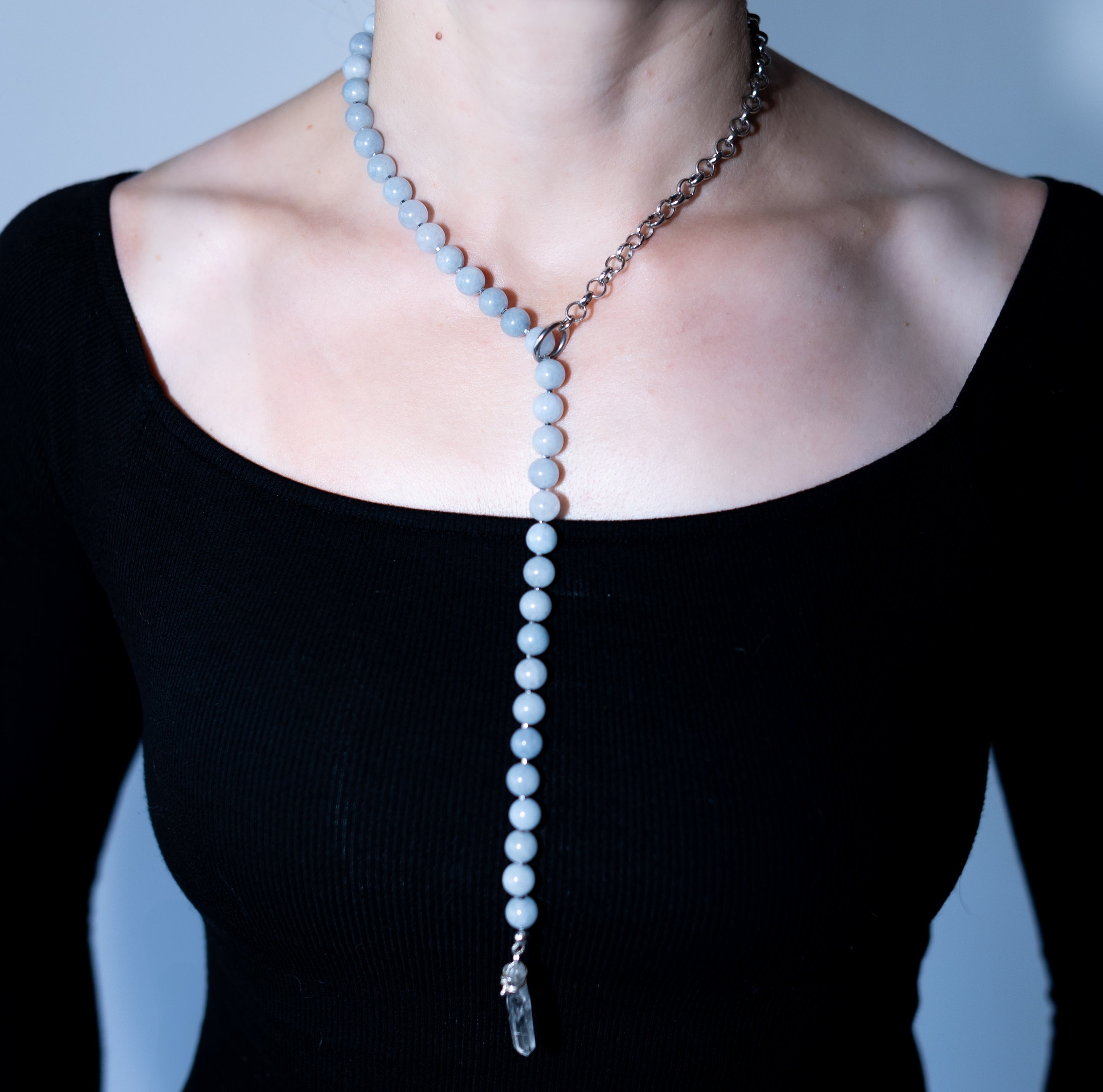 Necklace with blue beads and a chain on a black top against a gray background