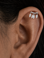 A close-up of a person's ear wearing a silver ear cuff with three dangling teardrop-shaped clear stones.