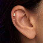 A close-up of a person's ear wearing a gold ear cuff with a marquise-cut clear stone and a small dangling clear stone.