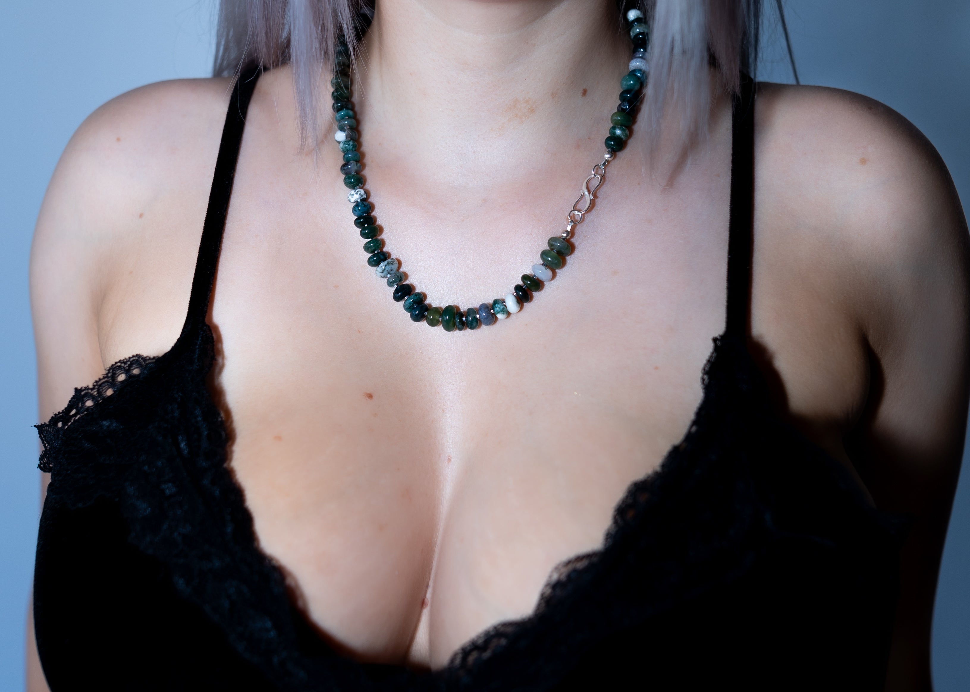 Person wearing a black lace top and green beaded necklace against a blue background