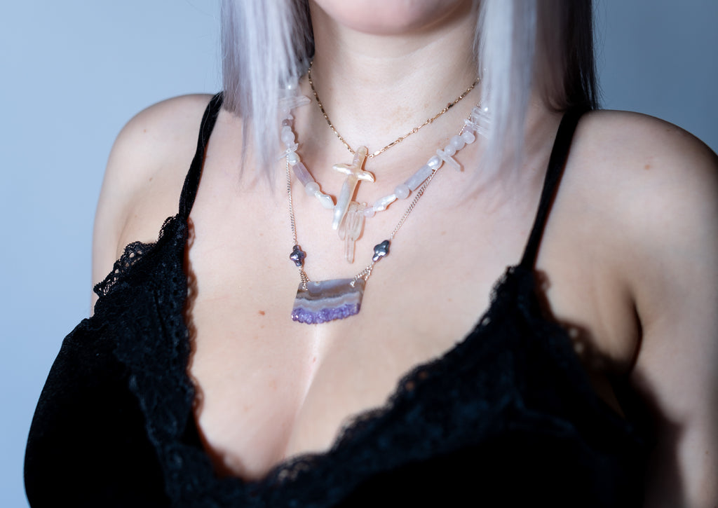 Person wearing a black lace top with multiple necklaces against a light blue background