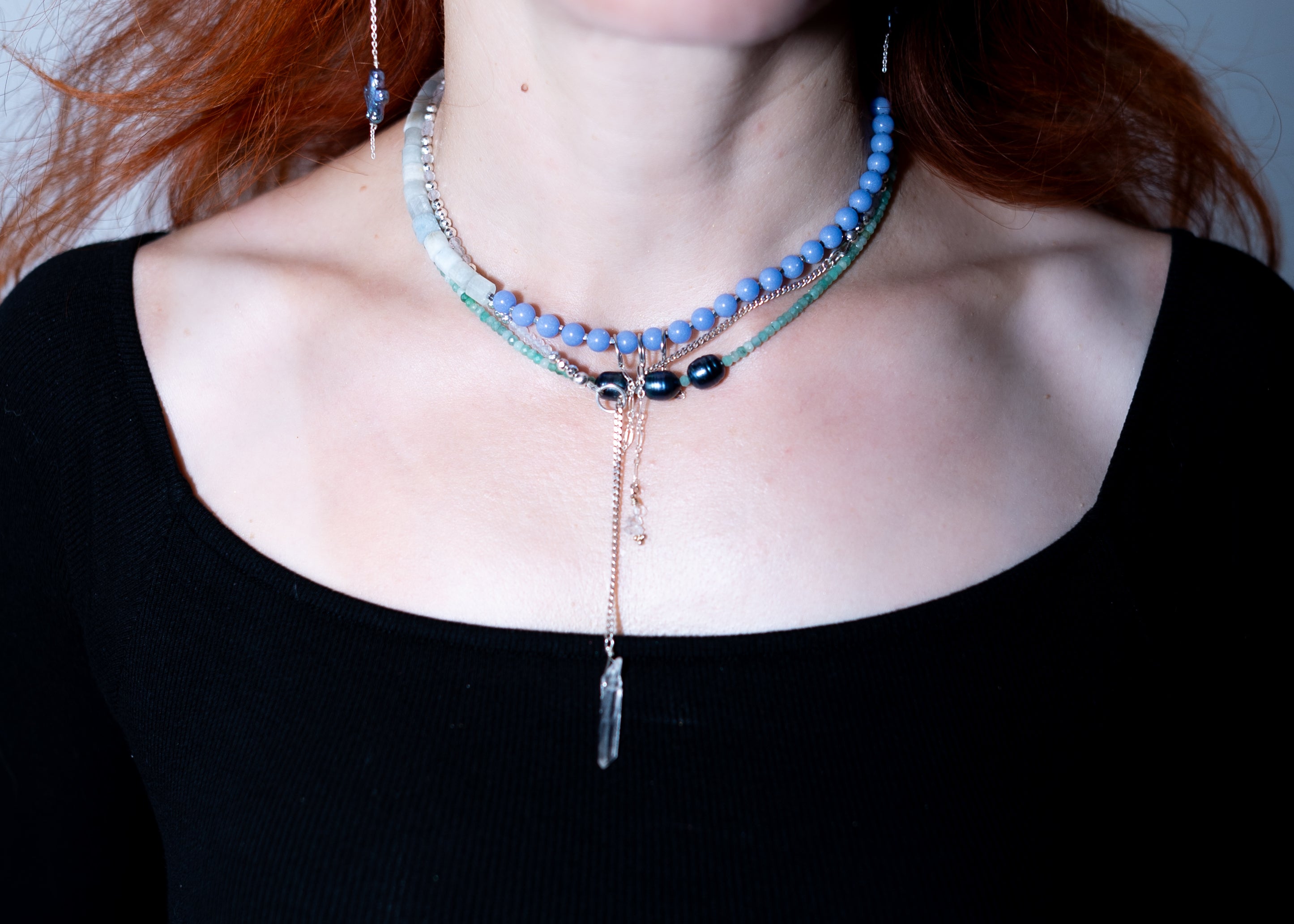 Necklace with blue beads and a pendant on a person wearing a black top.