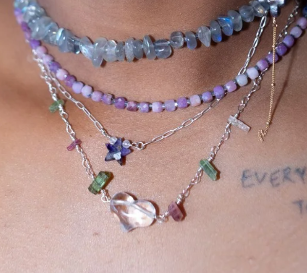 Close-up of layered necklaces with gemstones and charms on a person's neck.