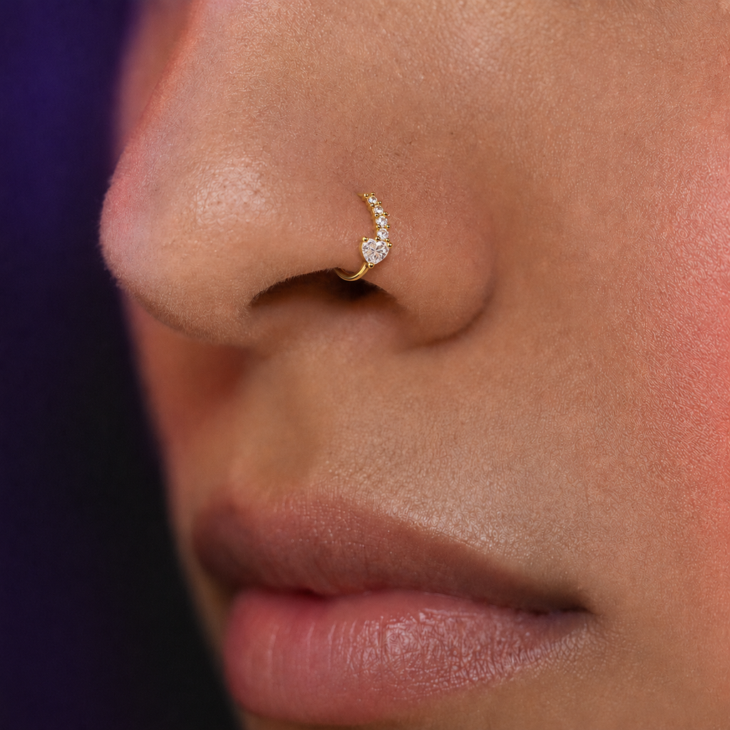 A close-up of a person's nose wearing a delicate gold crescent moon nose ring adorned with small clear stones.