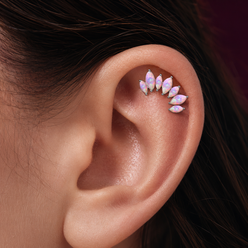 A close-up of a person's ear wearing a cluster of small marquise-shaped opal stud earrings in silver settings.