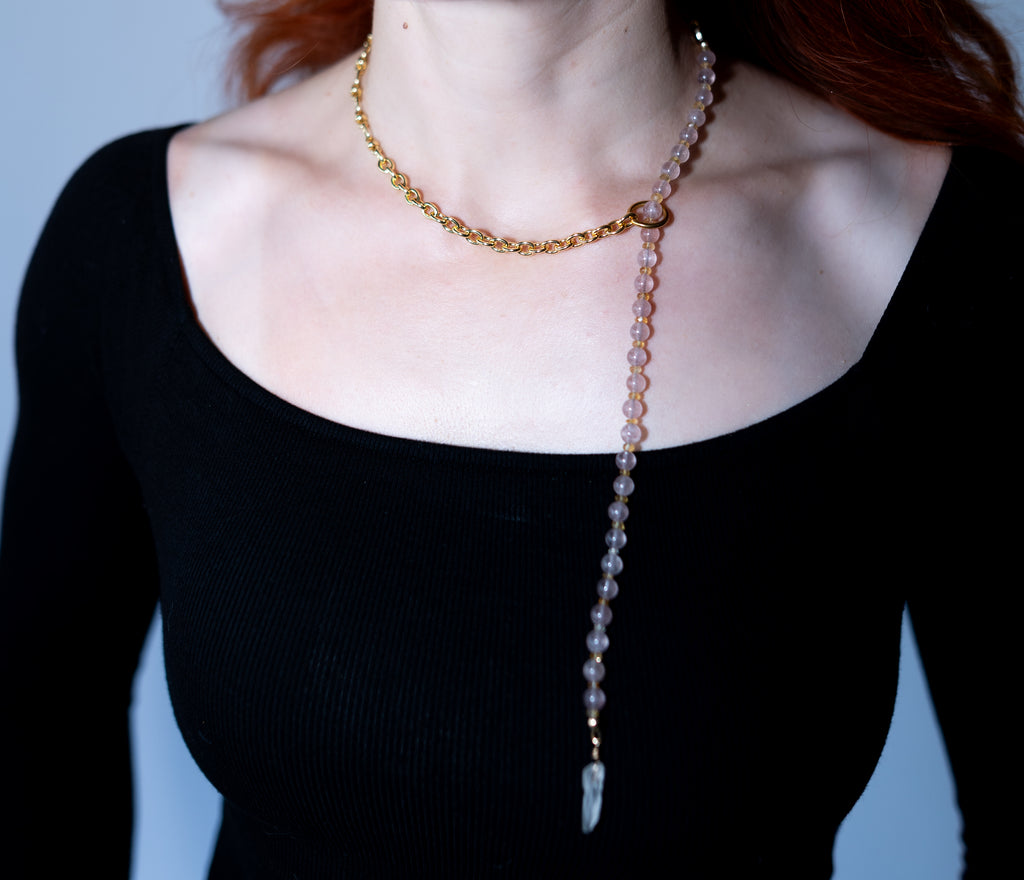 Person wearing a beaded necklace with a pendant on a plain background