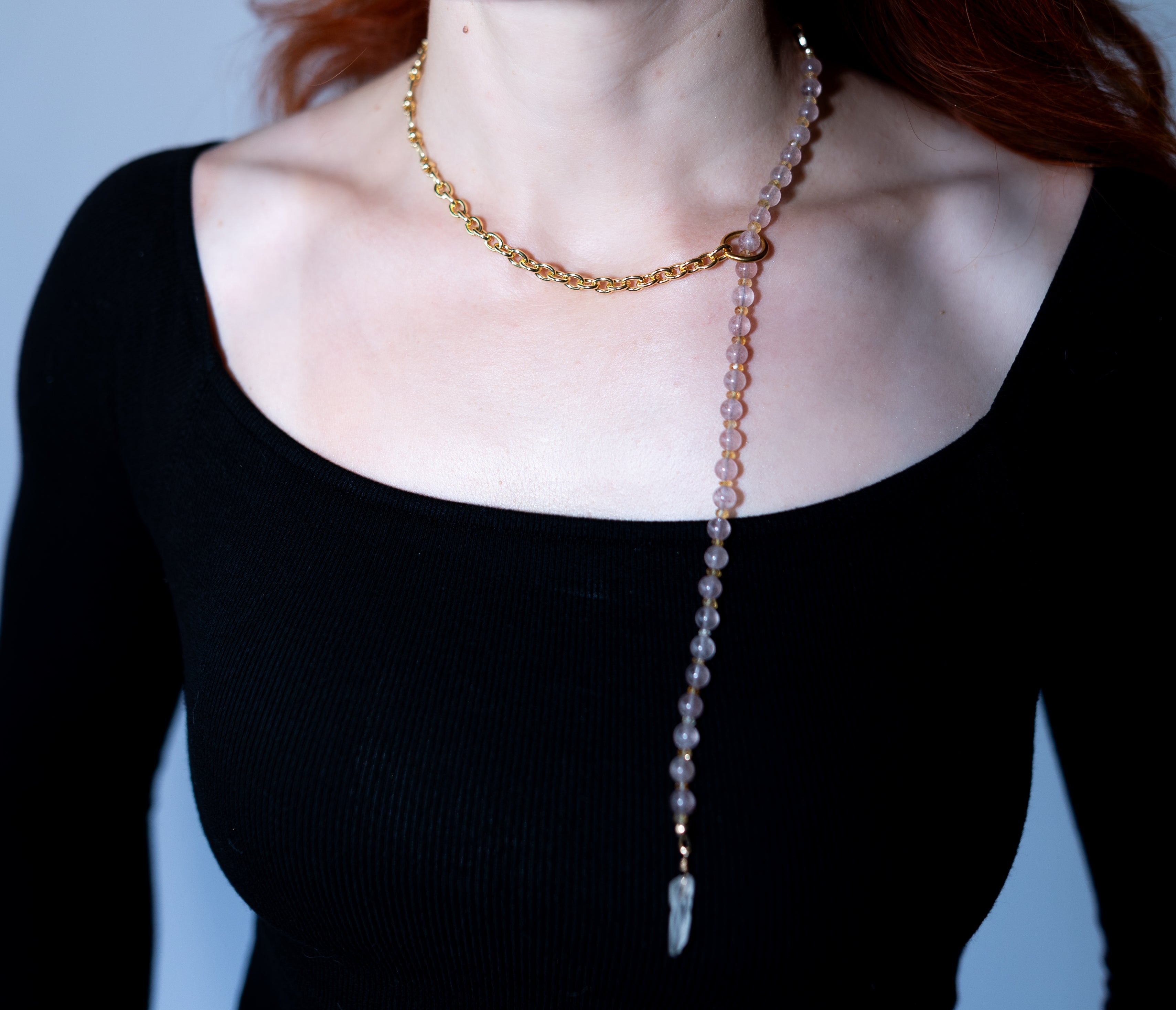 Person wearing a beaded necklace with a pendant on a plain background