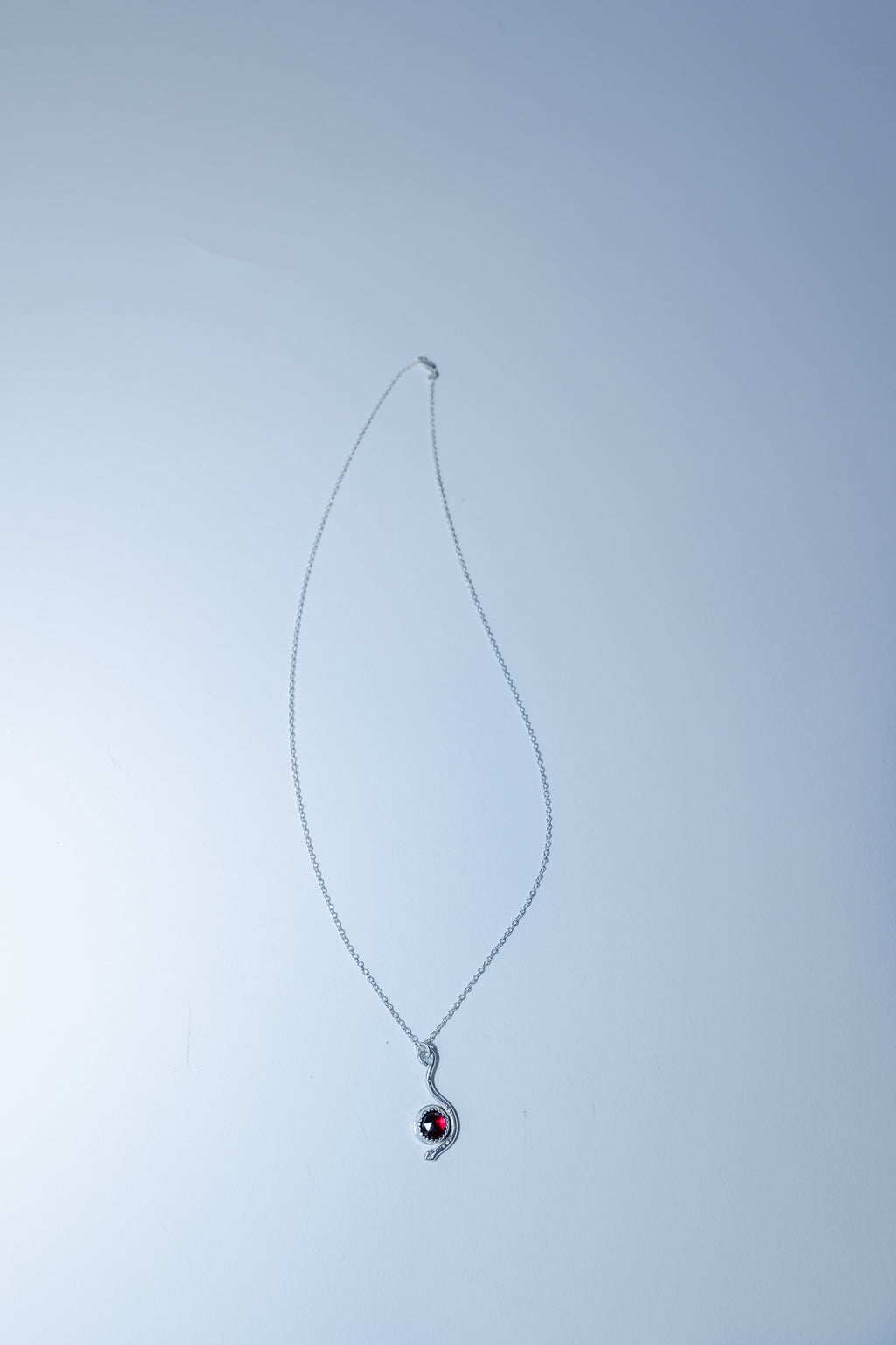 Silver necklace with a red gemstone pendant on a light gray background