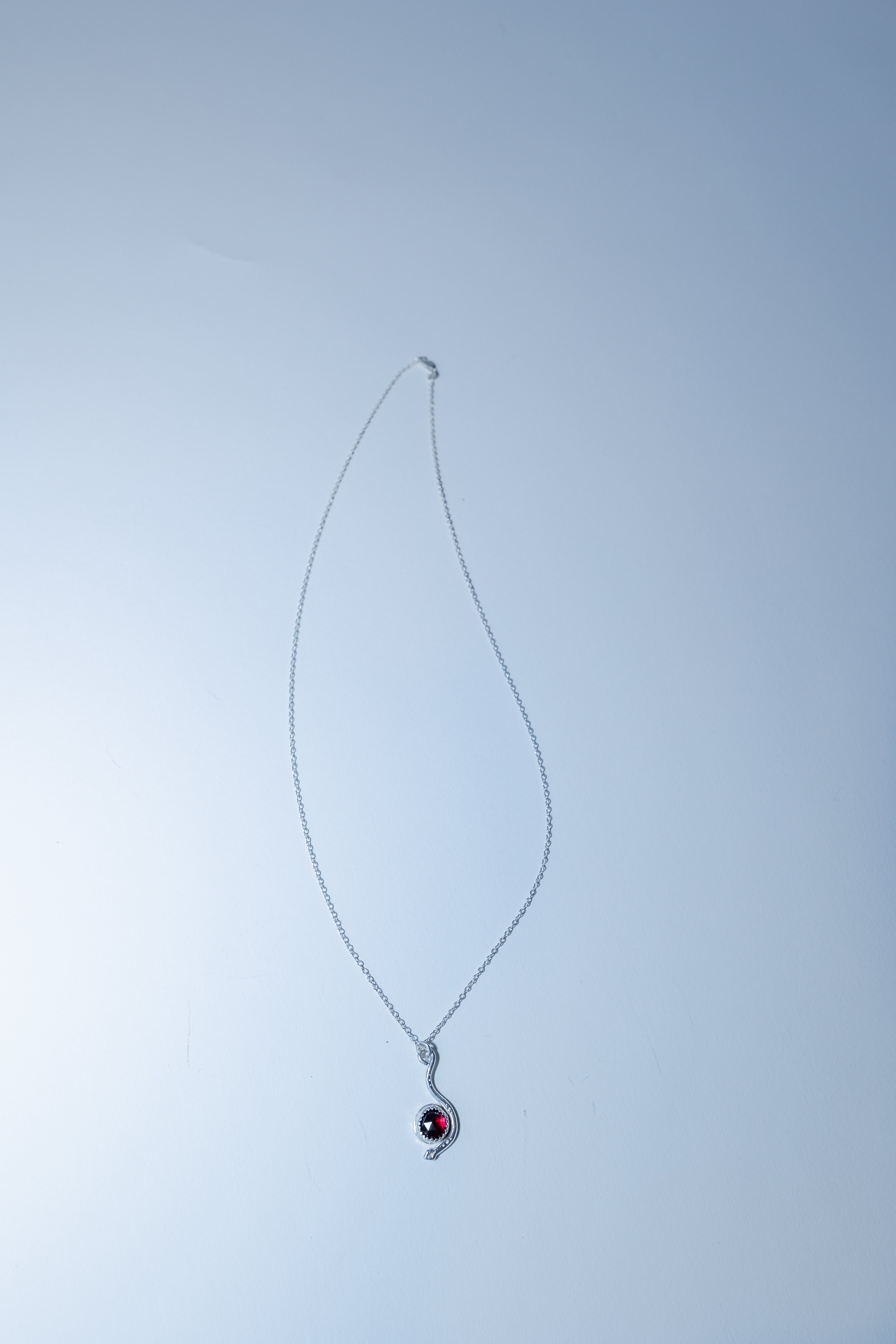 Silver necklace with a red gemstone pendant on a light gray background