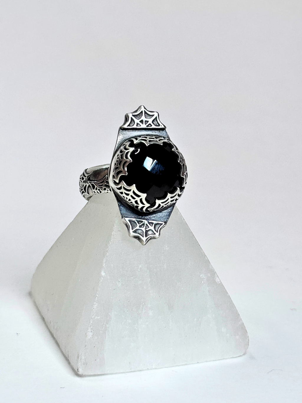 Silver ring with a black gemstone on a white stand against a white background
