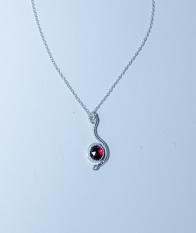 Silver necklace with a red gemstone pendant on a light gray background