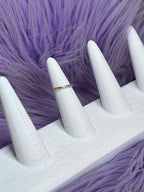 Gold ring on a white mannequin hand against a purple textured background