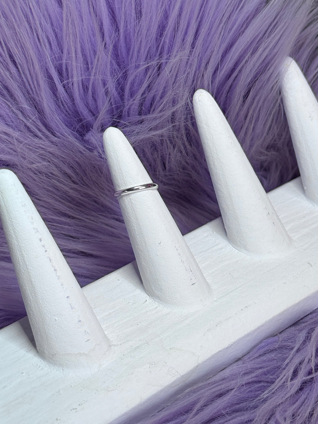 White stiletto nails with a ring on a purple textured background