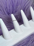 White stiletto nails with a ring on a purple textured background