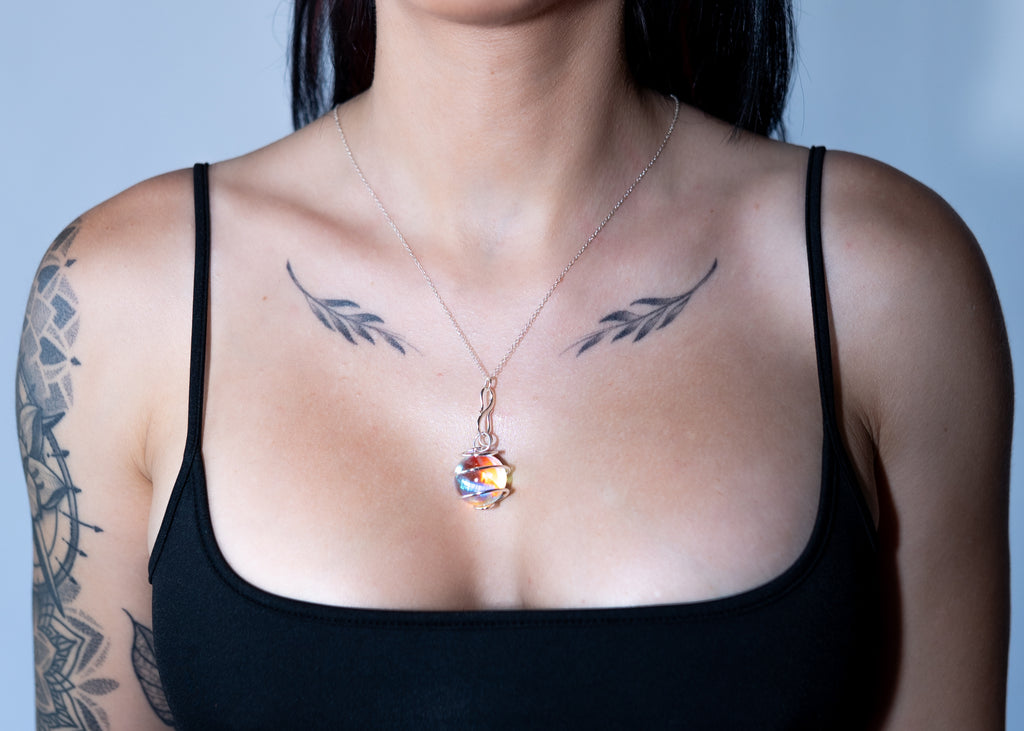 Person wearing a black tank top with tattoos on shoulders and chest, featuring a colorful pendant necklace.