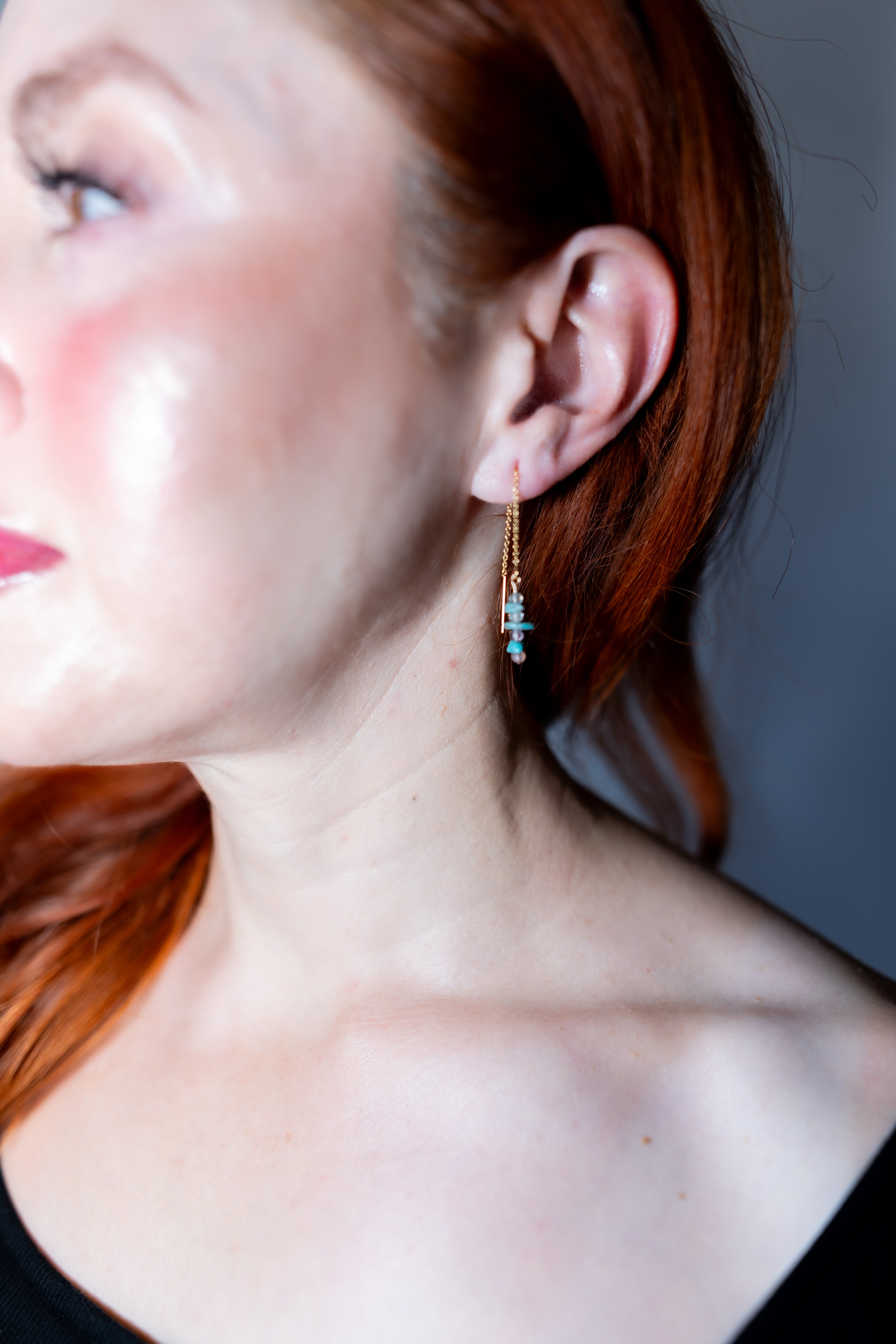 Close-up of a person wearing a delicate earring with turquoise stones.