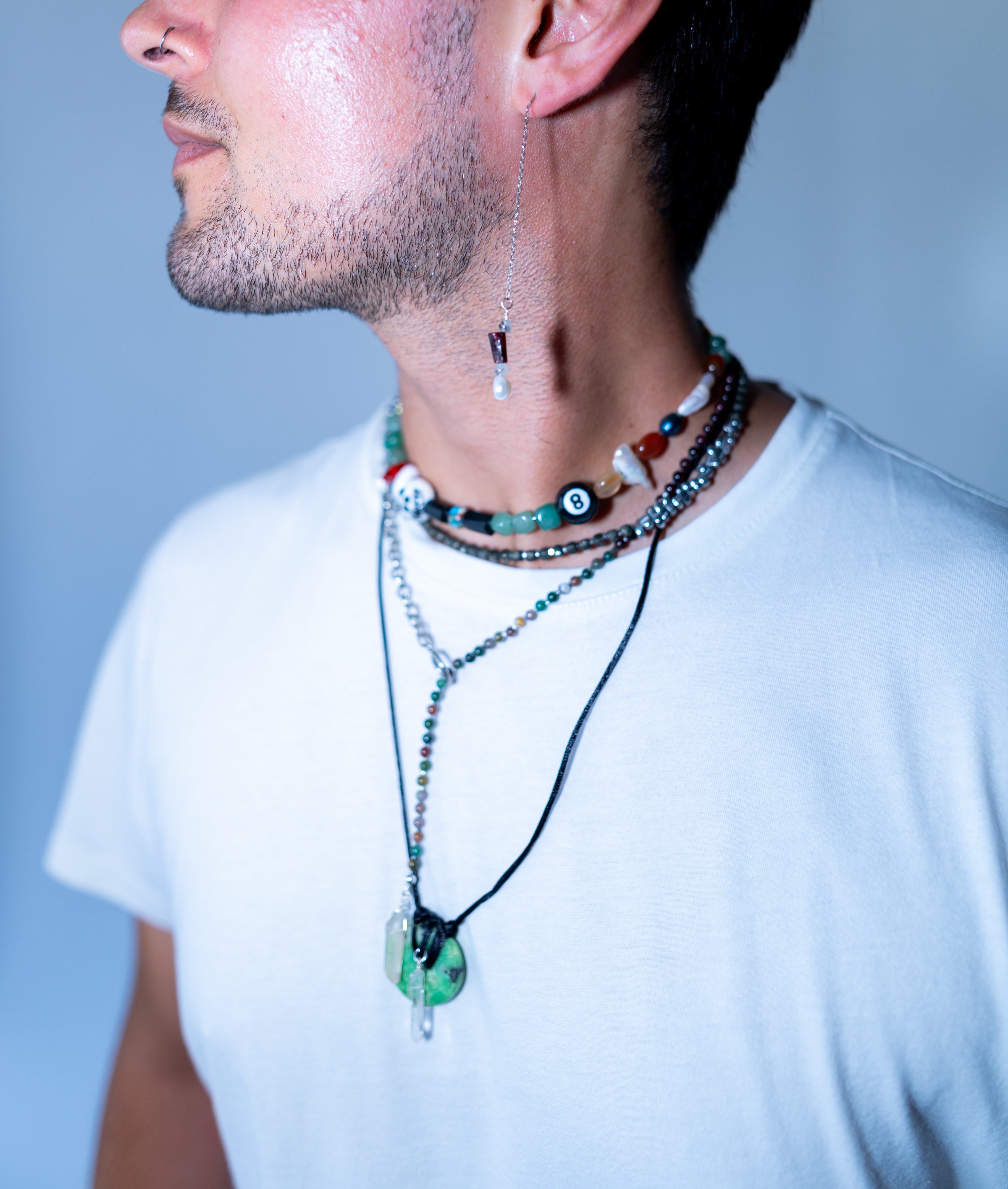 Man wearing multiple necklaces with various pendants on a plain background