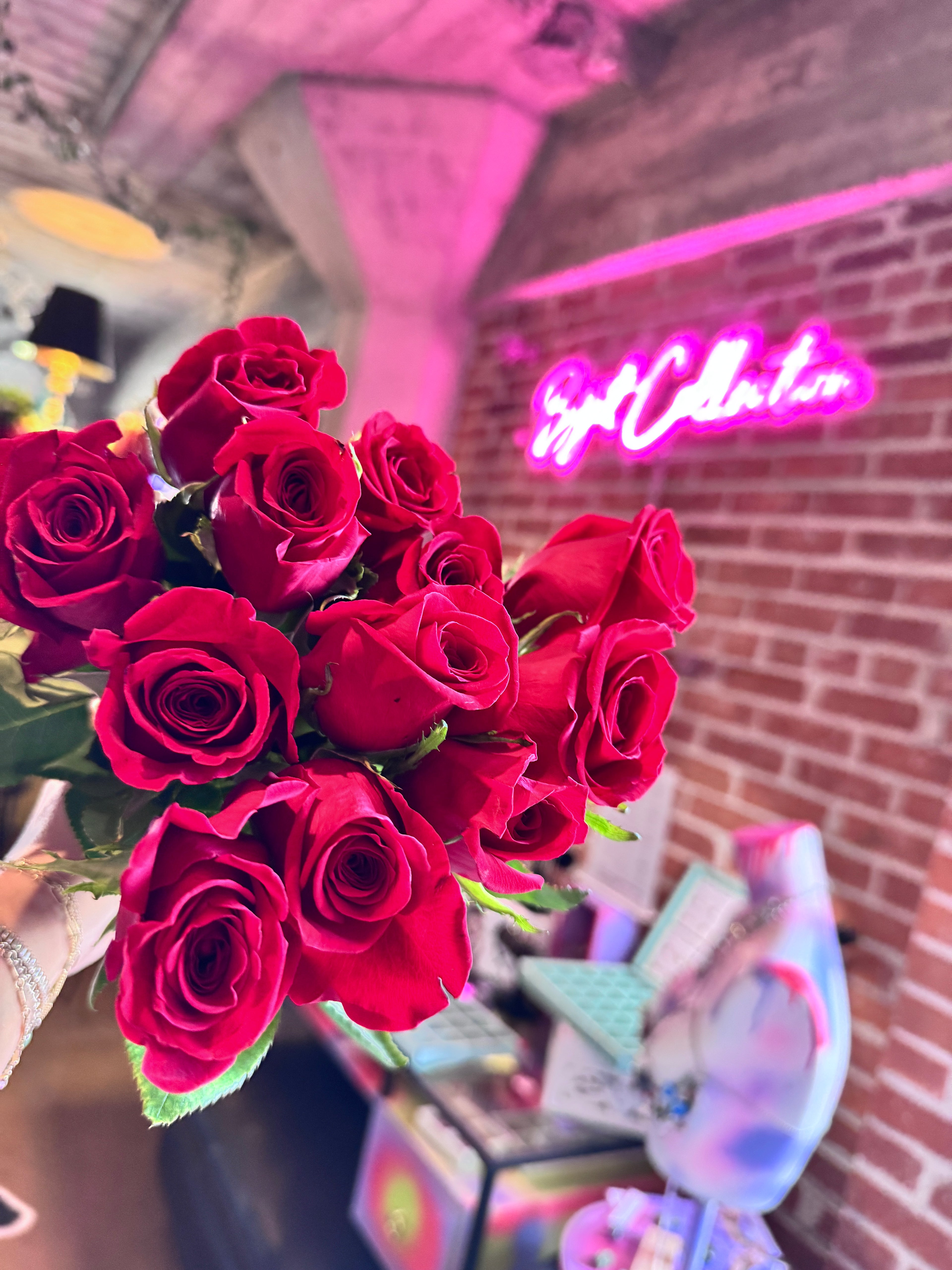 Bouquet of red roses held against a colorful, urban background with neon signs.